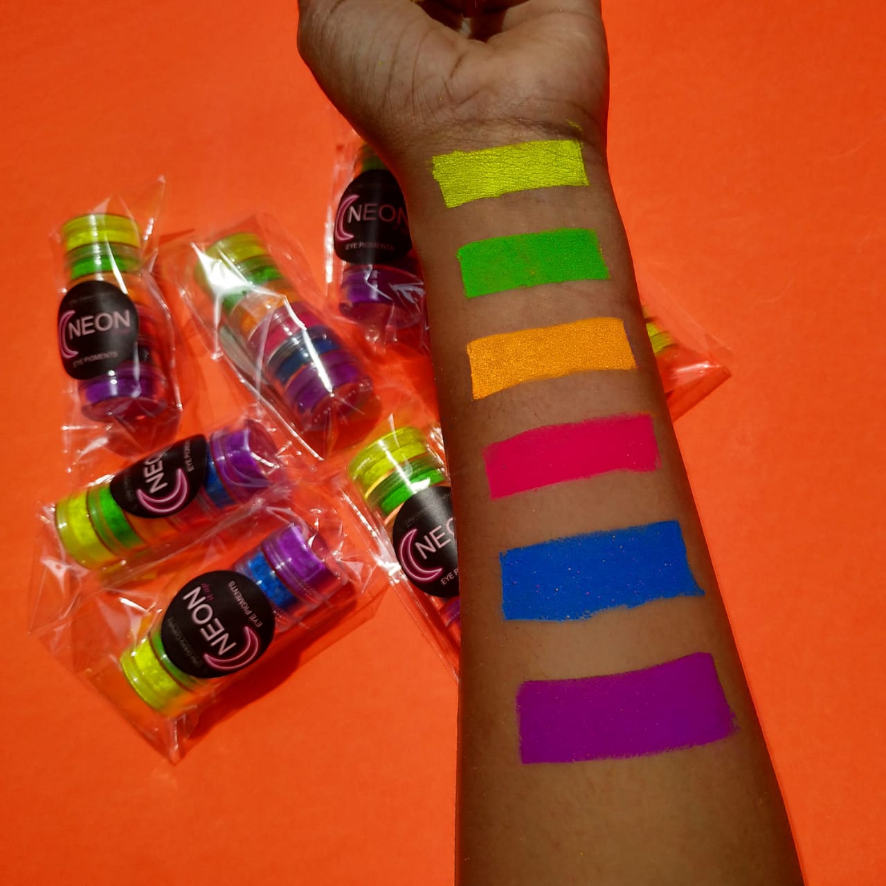 Glitter Galaxy Neon Eye Pigment swatches featuring vibrant yellow, green, orange, pink, blue, and purple neon eye makeup colors on arm.