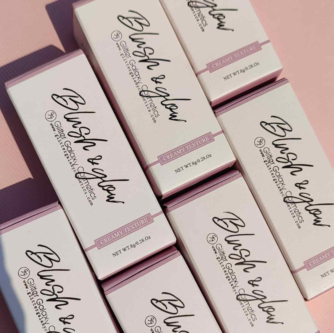 Glitter Galaxy Cosmetics Blush & Glow cream blush stick packaging featuring elegant pastel pink boxes with premium minimalist branding and creamy texture labeling.