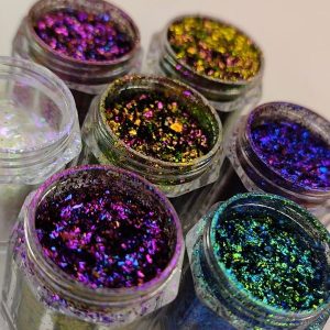 Glitter Galaxy Cosmetics multichrome glitter flakes collection featuring six premium cosmetic glitter jars with vibrant color-shifting flakes in purple, blue, green, gold, and iridescent finishes.